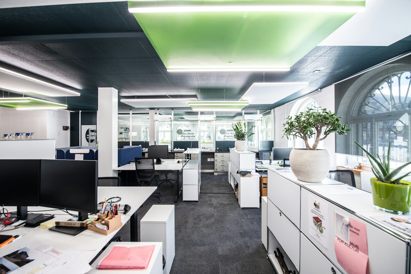 Moderno ufficio open space con postazioni di lavoro bianche e grandi finestre.