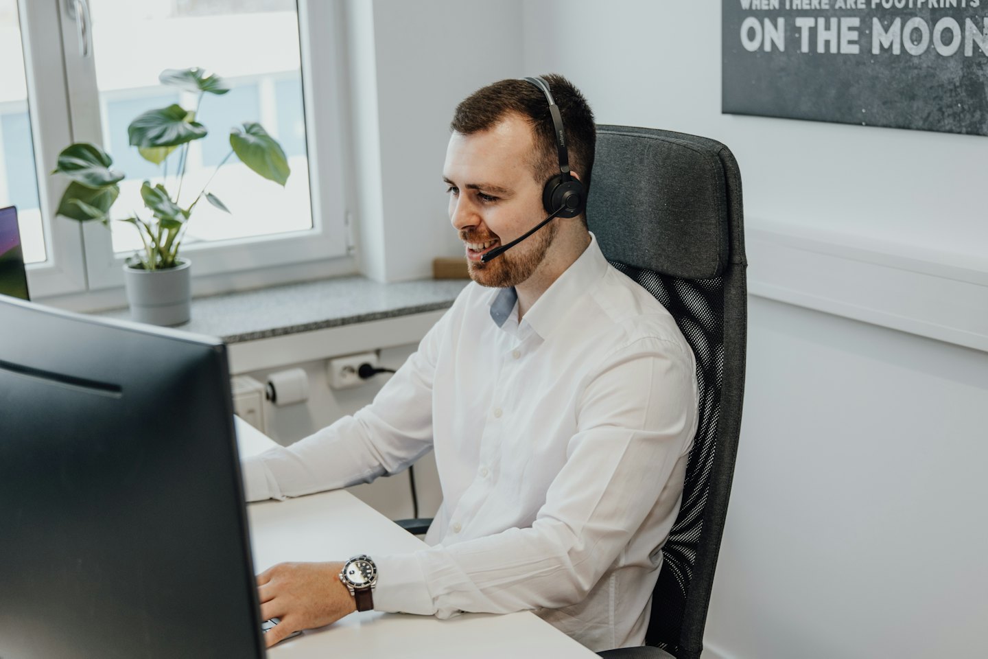 Un uomo con le cuffie sorride mentre lavora al computer.